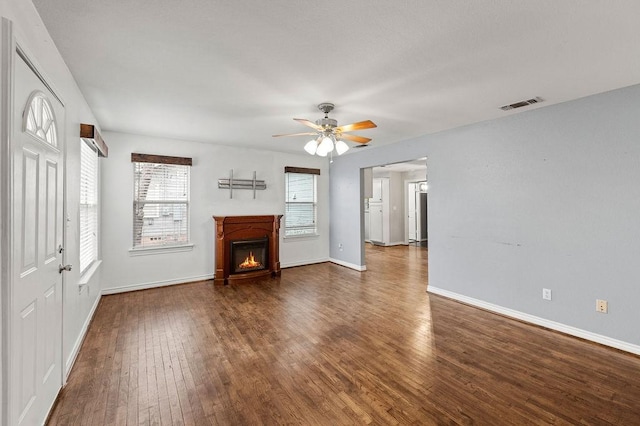 unfurnished living room with dark wood-style flooring, visible vents, a ceiling fan, a lit fireplace, and baseboards