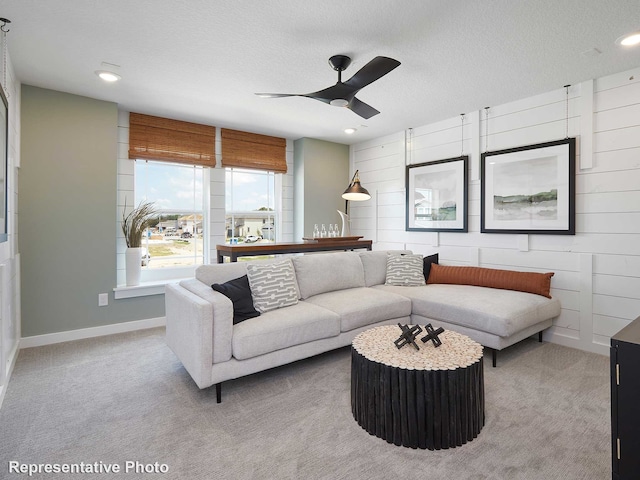 living area with a textured ceiling, carpet floors, ceiling fan, and baseboards