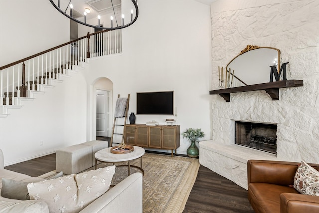 living room featuring arched walkways, a fireplace, an inviting chandelier, wood finished floors, and stairs