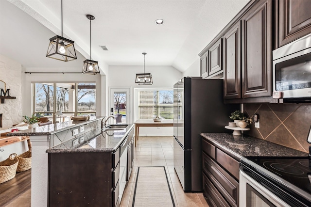 kitchen with dark stone counters, dark brown cabinets, appliances with stainless steel finishes, and a center island with sink