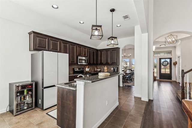 kitchen with arched walkways, dark brown cabinetry, stainless steel appliances, dark stone countertops, and an inviting chandelier