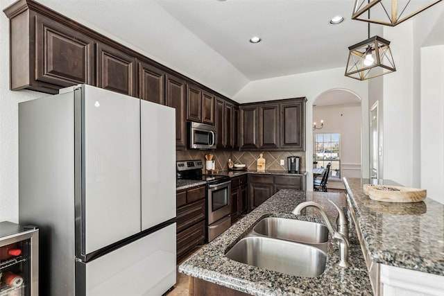 kitchen featuring dark stone counters, appliances with stainless steel finishes, hanging light fixtures, dark brown cabinets, and a sink