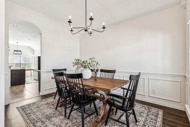 dining room featuring arched walkways, a decorative wall, a notable chandelier, and ornamental molding