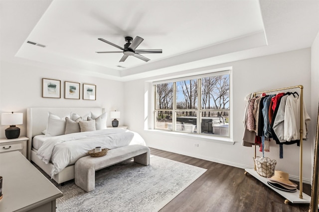 bedroom featuring dark wood-type flooring, a tray ceiling, visible vents, and a ceiling fan