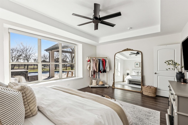 bedroom with a tray ceiling, dark wood finished floors, and a ceiling fan