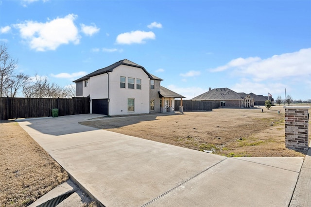 view of front of house featuring driveway, an attached garage, fence, and stucco siding