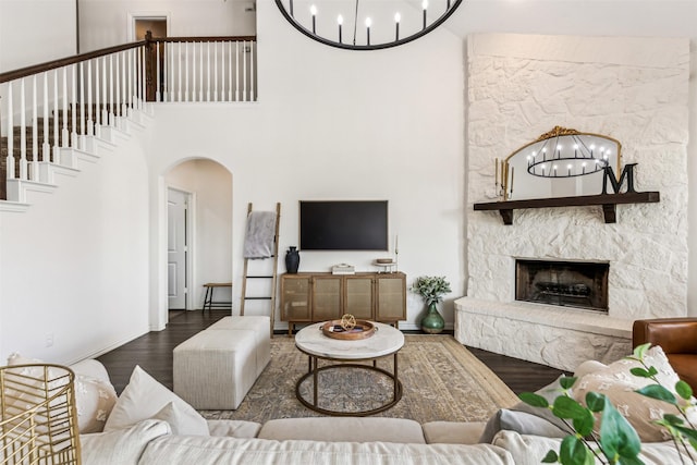 living room with arched walkways, a high ceiling, a stone fireplace, wood finished floors, and baseboards