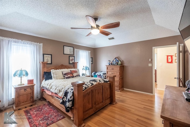 bedroom featuring a textured ceiling, ceiling fan, visible vents, baseboards, and light wood finished floors