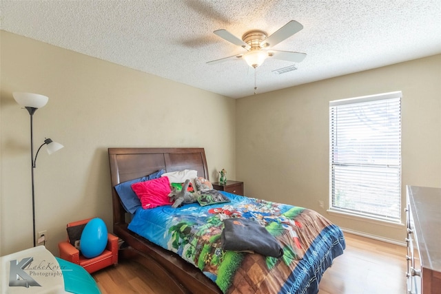 bedroom featuring a textured ceiling, multiple windows, wood finished floors, and visible vents