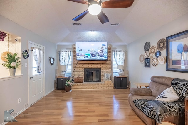 living area featuring lofted ceiling, light wood-type flooring, visible vents, and a brick fireplace