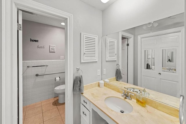 bathroom with tile walls, toilet, wainscoting, vanity, and tile patterned flooring