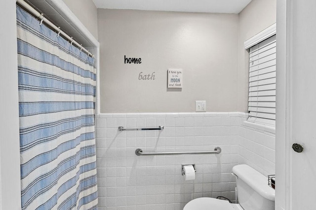 bathroom featuring wainscoting, tile walls, and toilet