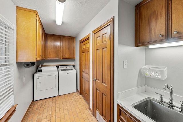 laundry area with brick floor, cabinet space, a sink, a textured ceiling, and washer and dryer