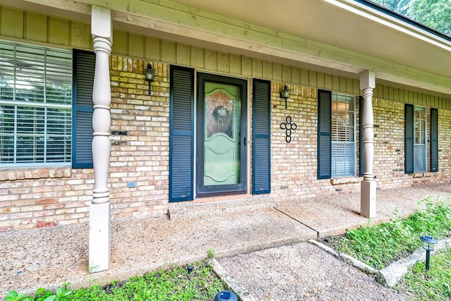 entrance to property featuring covered porch, brick siding, and board and batten siding