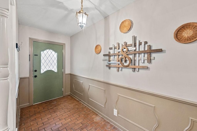 foyer entrance with brick floor and a wainscoted wall