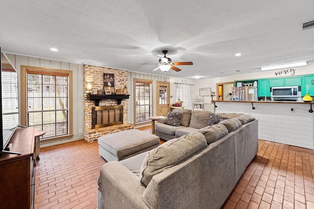 living area with a ceiling fan, brick floor, a textured ceiling, a brick fireplace, and recessed lighting