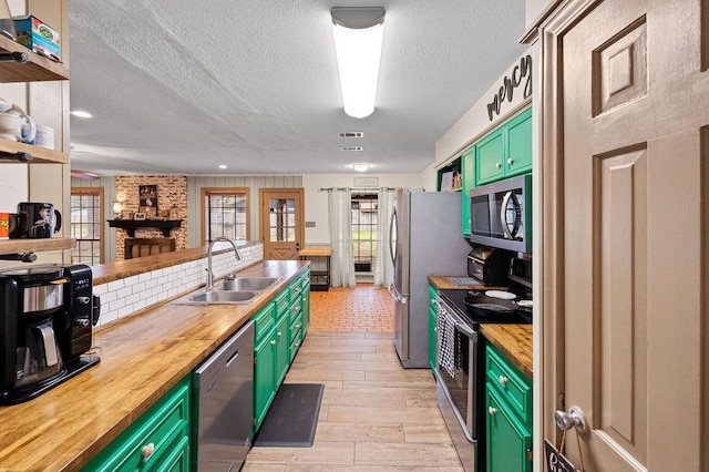 kitchen featuring stainless steel appliances, a sink, green cabinets, wooden counters, and light wood finished floors