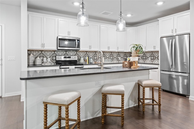 kitchen featuring dark countertops, a kitchen island with sink, stainless steel appliances, white cabinetry, and a sink