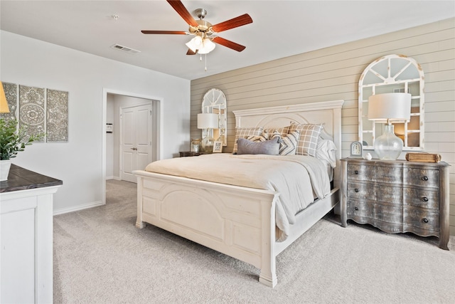 bedroom featuring light carpet, wood walls, visible vents, baseboards, and a ceiling fan