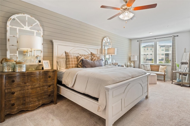 bedroom with a ceiling fan, light carpet, and wood walls