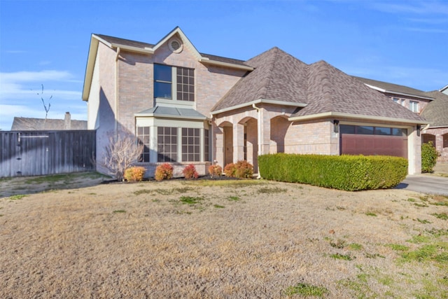 traditional-style house featuring a garage, brick siding, fence, driveway, and roof with shingles