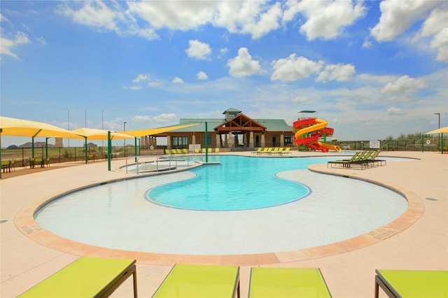 community pool with playground community, a water slide, a patio area, and fence