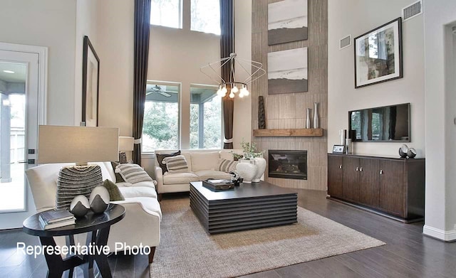 living area featuring dark wood-style flooring, visible vents, a tiled fireplace, and a high ceiling