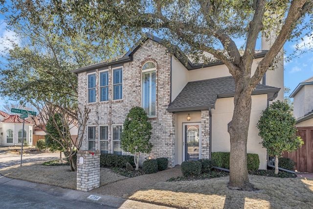 traditional home featuring a shingled roof, brick siding, fence, and stucco siding