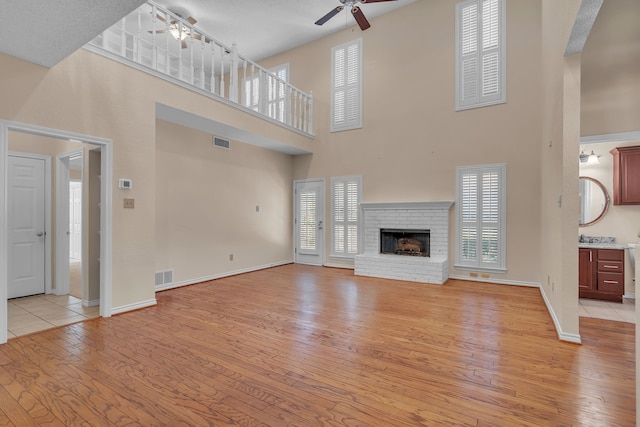 unfurnished living room with light wood-style floors, ceiling fan, a fireplace, and visible vents