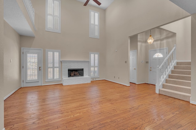 unfurnished living room with ceiling fan, baseboards, stairway, light wood-type flooring, and a brick fireplace