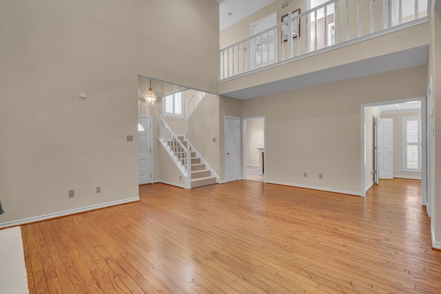 unfurnished living room featuring stairway, a wealth of natural light, light wood-style flooring, and baseboards