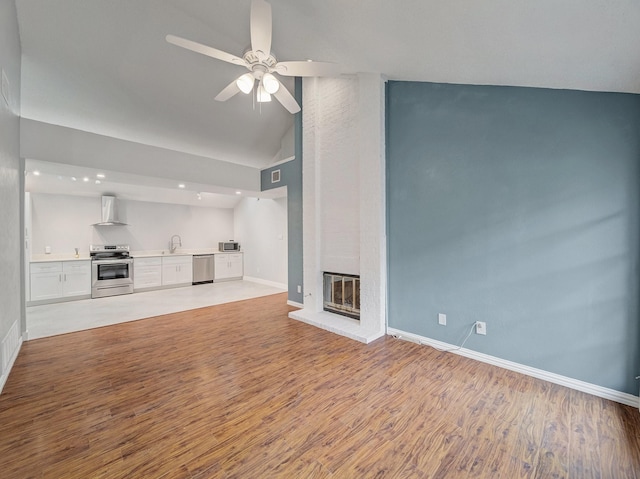 unfurnished living room with a brick fireplace, baseboards, a sink, and wood finished floors