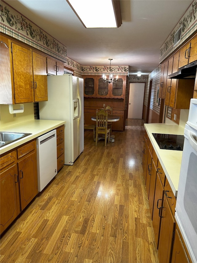 kitchen featuring hanging light fixtures, white appliances, brown cabinetry, and light countertops