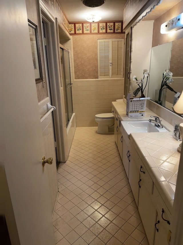 full bath featuring vanity, tile walls, wainscoting, tile patterned floors, and wallpapered walls