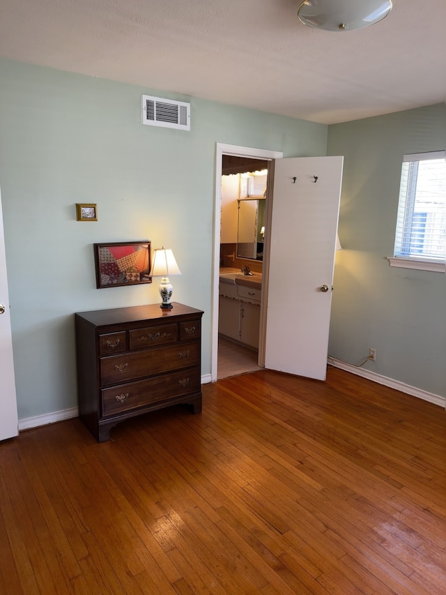 bedroom featuring connected bathroom, a sink, wood finished floors, visible vents, and baseboards