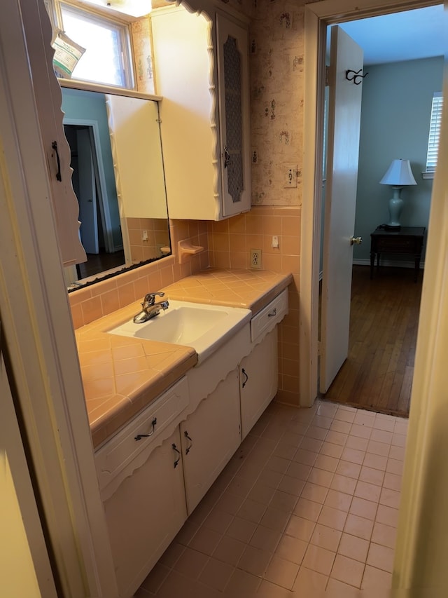 bathroom with tile walls, wallpapered walls, wainscoting, vanity, and tile patterned floors