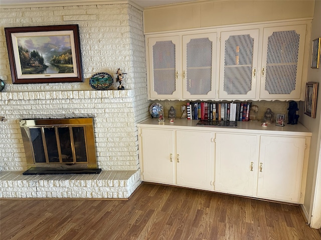 interior space with dark wood-style floors, light countertops, glass insert cabinets, a brick fireplace, and white cabinets