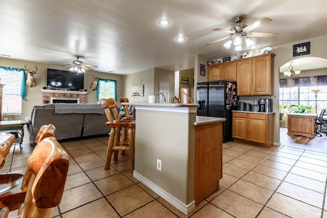 kitchen with ceiling fan with notable chandelier, a kitchen breakfast bar, open floor plan, light countertops, and black fridge