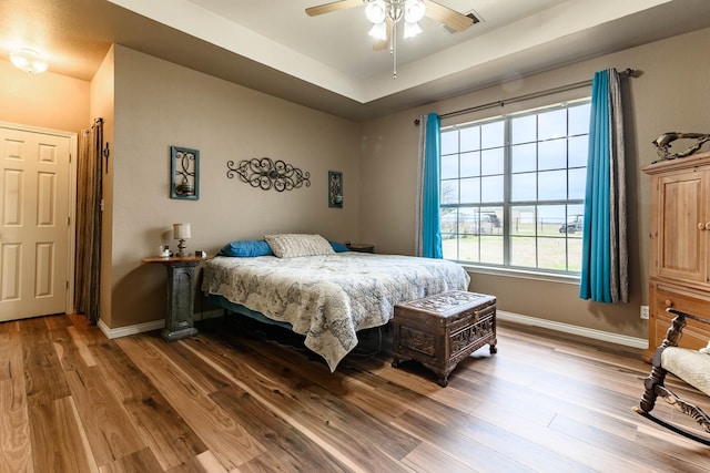 bedroom featuring a raised ceiling, baseboards, and wood finished floors