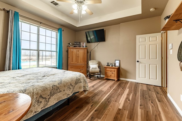 bedroom featuring wood finished floors, a raised ceiling, visible vents, and baseboards