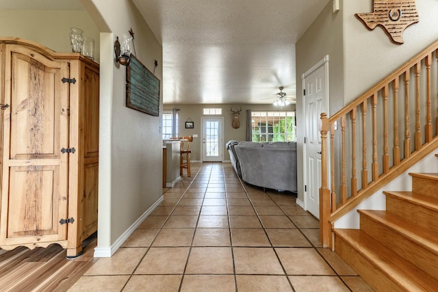 foyer entrance with stairway, a textured ceiling, baseboards, and light tile patterned floors