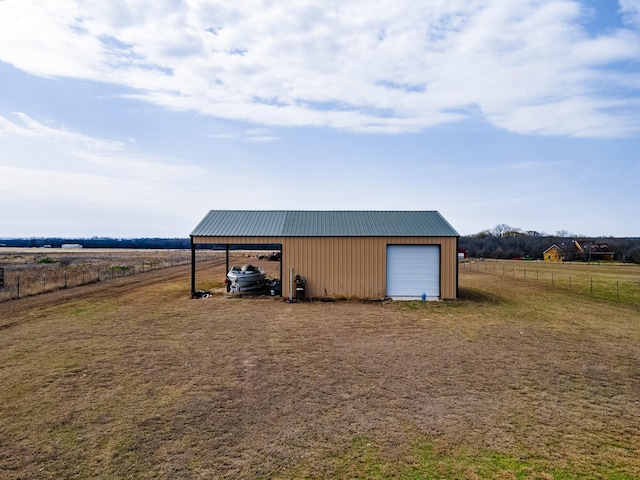 view of outdoor structure featuring a rural view, fence, driveway, and an outdoor structure