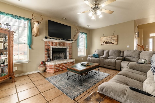 living area featuring light tile patterned floors, visible vents, a ceiling fan, a brick fireplace, and baseboards