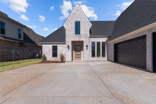 french country inspired facade featuring a shingled roof, concrete driveway, and brick siding