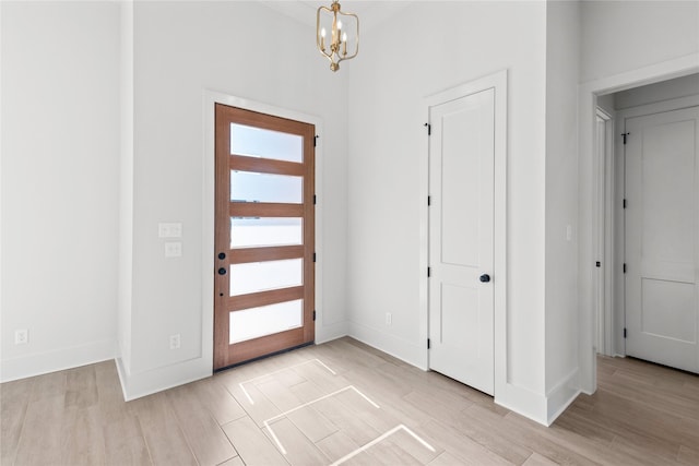 foyer entrance with light wood-type flooring, baseboards, and an inviting chandelier