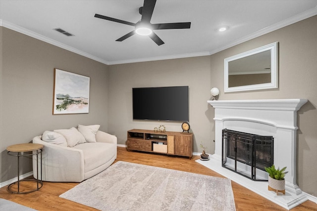 living room featuring light wood-type flooring, visible vents, a fireplace with raised hearth, and crown molding