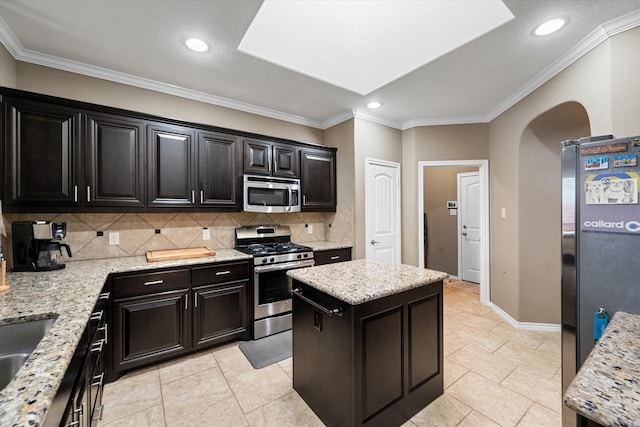 kitchen featuring appliances with stainless steel finishes, a center island, arched walkways, and light stone counters