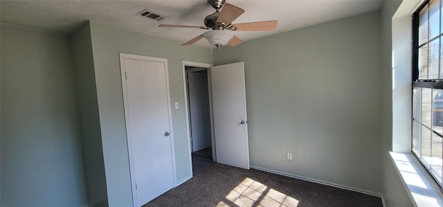 unfurnished bedroom with a textured ceiling, dark carpet, visible vents, and a ceiling fan