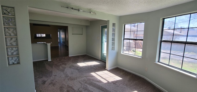 empty room featuring a textured ceiling, dark carpet, and baseboards