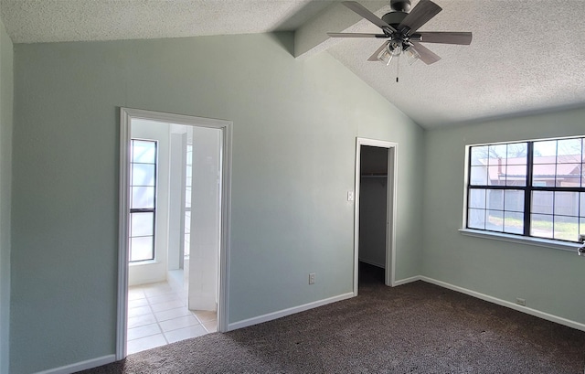 unfurnished bedroom featuring a walk in closet, light carpet, vaulted ceiling, a textured ceiling, and baseboards